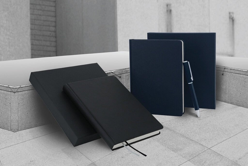 Lifestyle example of two sets of notebooks, navy and black with a navy metal ballpoint pen